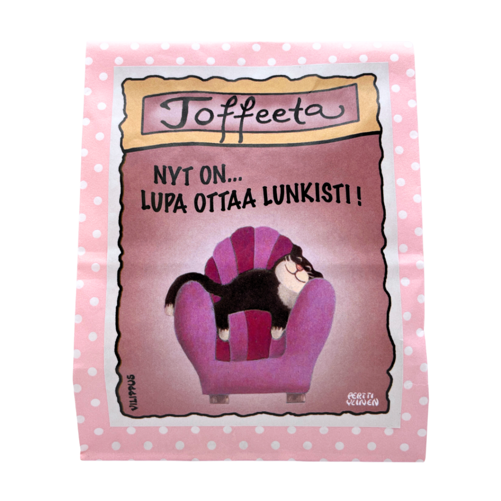 Kermatoffee vaaleanpunaisessa paperipussissa, jonka etiketissä kuvitus nojatuolissa loikoilevasta kissasta, sekä teksti "Nyt on lupa ottaa lunkisti!"