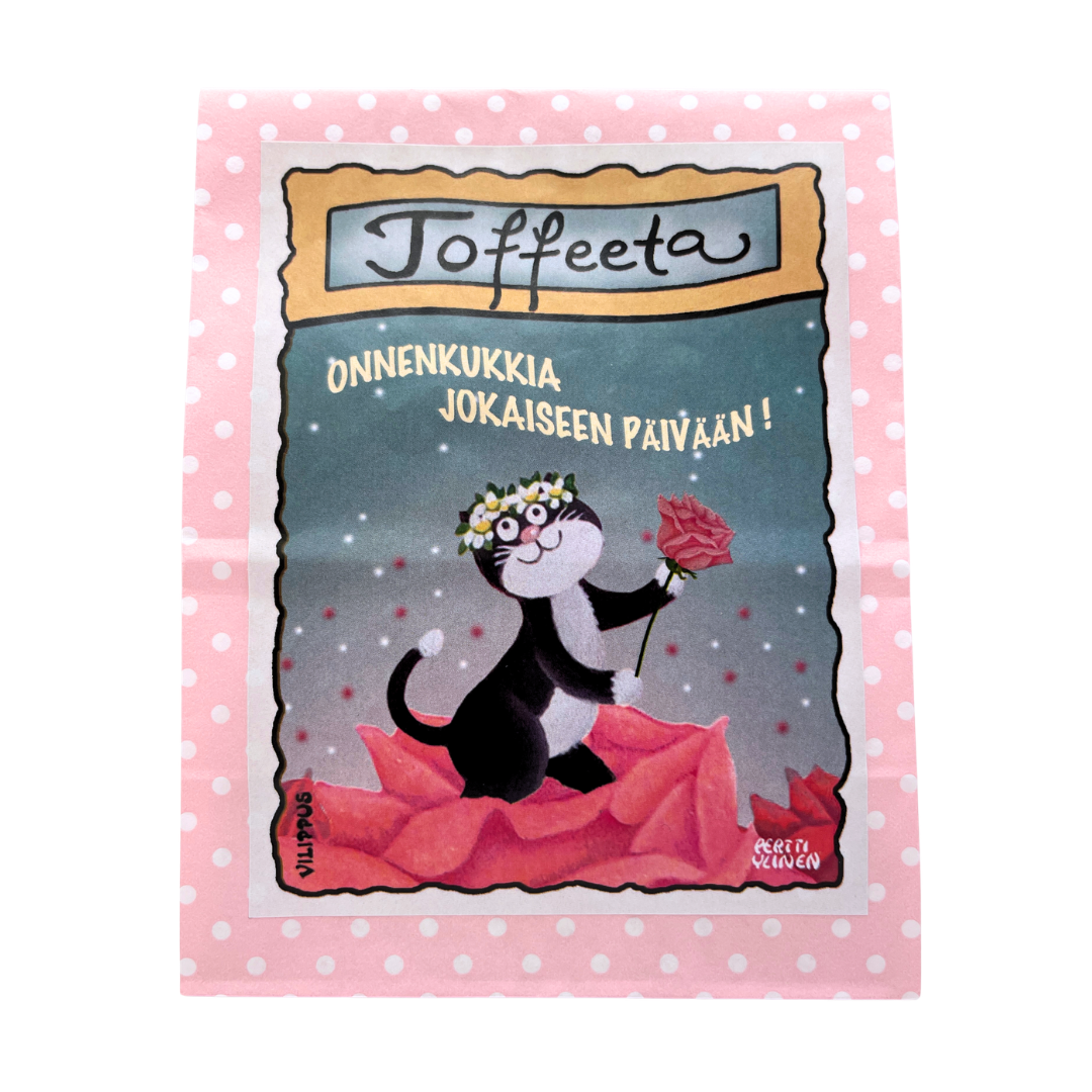 Kermatoffee vaaleanpunaisessa paperipussissa, jonka etiketissä kuvitus ruusua ojentavasta kissasta, sekä teksti "Onnenkukkia jokaiseen päivään!"